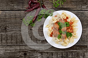 Pasta Conchiglie and meatballs with tomato sauce on rustic wooden background. Top view