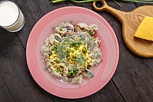 Pasta in a creamy sauce with mushrooms in a plate on a dark wooden table next to a glass of cream, cheese and mushrooms
