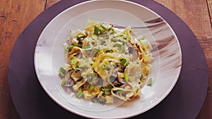 Pasta in a creamy sauce with mushrooms in a plate rotates in a circle on a black background