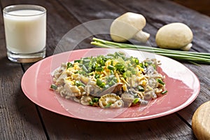 Pasta in a creamy sauce with mushrooms in a plate on the table next to a glass of cream, green onions and champignons