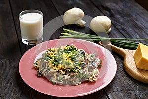 Pasta in a creamy sauce with mushrooms in a plate on the table next to a glass of cream, green onions and champignons.