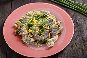 Pasta in a creamy sauce with mushrooms in a plate on the table next to green onion feathers