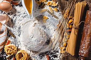 Pasta on dark wooden background with dough, eggs, oil and flour close-up macro