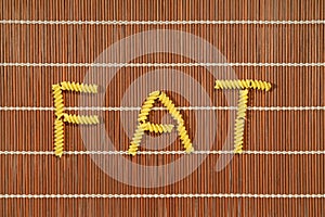 Pasta elements forming word FAT on brown table set