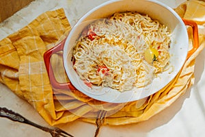 Pasta from feta cheese with small tomatoes in olive oil with herbs and spices in ceramic baking dish with yellow cotton napkin.