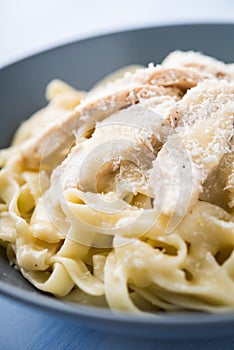 Pasta fettuccine alfredo with chicken and parmesan on blue wooden background close up