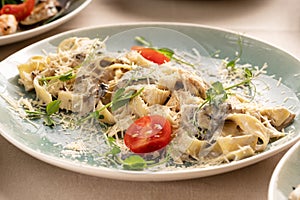 Pasta fettuccine with mushrooms and fried chicken meat in creamy sauce garnished tomatoes on a light table in restaurant