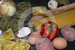 Pasta food background with a copy space of ravioli, spaghetti,egg,potato,tomato and a wood kneader on floury black background