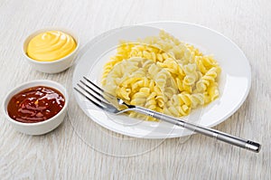 Pasta fusilli, fork in plate, ketchup and mayonnaise on table