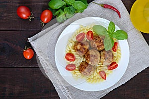 Pasta futsilli with meat balls, cherry tomatoes, basil on a white plate on a dark wooden background.
