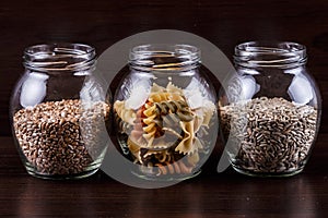 Pasta and grains of dry wheat in a jar on dark wooden background close-up macro