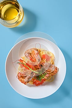 Pasta with langoustines and red caviar with a glass of white wine on a blue background.