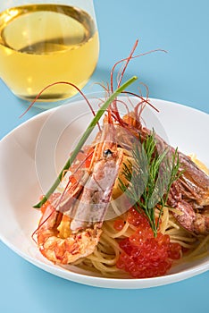 Pasta with langoustines and red caviar with a glass of white wine on a blue background.