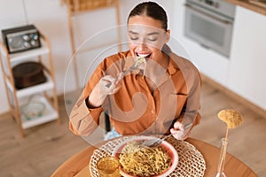 Pasta lover. Happy european woman eating tasty homemade spaghetti, enjoying delicious lunch in kitchen, above view