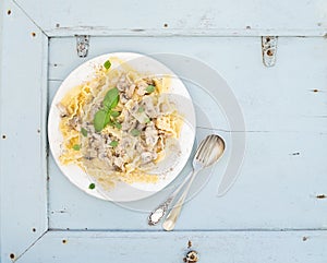 Pasta mafaldine with mushrooms and cream sauce in white ceramic plate over light blue wooden background. Top view.