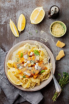 Pasta Mafaldine Napoletane with baked pumpkin, feta cheese and seasoning herbs in ceramic plate on gray concrete old background.