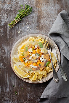 Pasta Mafaldine Napoletane with baked pumpkin, feta cheese and seasoning herbs in ceramic plate on gray concrete old background.