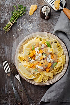 Pasta Mafaldine Napoletane with baked pumpkin, feta cheese and seasoning herbs in ceramic plate on gray concrete old background.