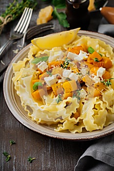 Pasta Mafaldine Napoletane with baked pumpkin, feta cheese and seasoning herbs in ceramic plate on gray concrete old background.