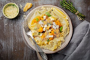 Pasta Mafaldine Napoletane with baked pumpkin, feta cheese and seasoning herbs in ceramic plate on gray concrete old background.