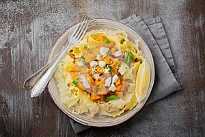 Pasta Mafaldine Napoletane with baked pumpkin, feta cheese and seasoning herbs in ceramic plate on gray concrete old background.