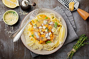 Pasta Mafaldine Napoletane with baked pumpkin, feta cheese and seasoning herbs in ceramic plate on gray concrete old background.