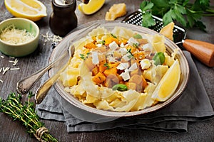 Pasta Mafaldine Napoletane with baked pumpkin, feta cheese and seasoning herbs in ceramic plate on gray concrete old background.