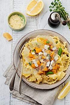 Pasta Mafaldine Napoletane with baked pumpkin, feta cheese and seasoning herbs in ceramic plate on white wooden background.