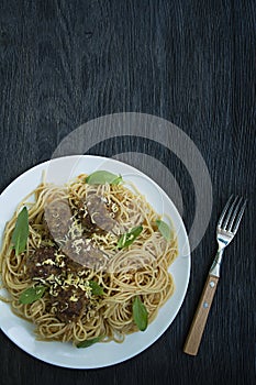 Pasta with meatballs and parsley in tomato sauce. Dark wooden background. View from above