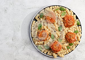 Pasta with meatballs in tomato sauce on a round plate on a light gray background