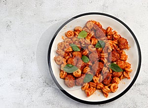 Pasta with meatballs in tomato sauce on a round plate on a light gray background