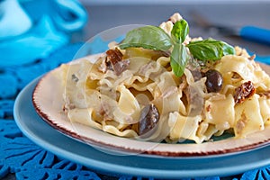 Pasta with olives, tuna, sun dried tomatoes and olive oil in a white and blue plate on a blue cloth.