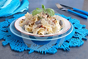 Pasta with olives, tuna, sun dried tomatoes and olive oil in a white and blue plate on a blue cloth.