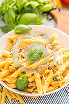Pasta penne with chicken pieces mushrooms basil parmesan cheese and white wine. Italian food in white plate on kitchen