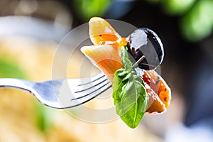 Pasta Penne with Tomato Bolognese Sauce, Parmesan Cheese black olive and Basil on a Fork. Mediterranean food.Italian cuisine