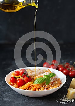 Pasta penne with tomato sauce, fresh basil, pouring olive oil and parmesan on the dark background