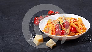 Pasta penne with tomato sauce, fresh basil, roasted tomatoes and parmesan on the dark background