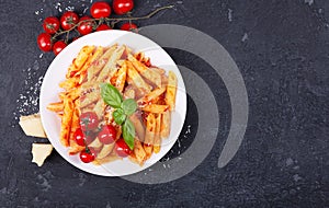 Pasta penne with tomato sauce, fresh basil, roasted tomatoes and parmesan on the dark background