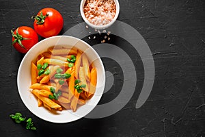 Pasta Penne in tomato sauce Pomodoro, garnished green basil leaves on black table. Traditional italian food. Top view