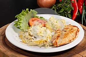 Pasta, penne in white sauce with cheese, accompanied by a salad of tomatoes, lettuce and cauliflower and grilled chicken file