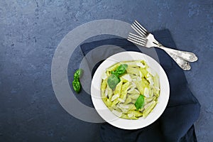 Pasta with pesto sauce decorated basil leaves and parmesan cheese in white dish on table above with empty space for you recipe.