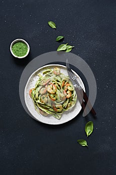 Pasta with pesto and shrimp on a plate on the kitchen table, top view