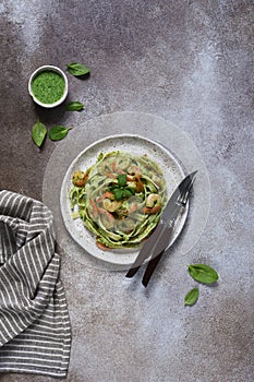 Pasta with pesto and shrimp on a plate on the kitchen table, top view