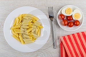 Pasta in plate, fork, tomatoes and boiled eggs in saucer