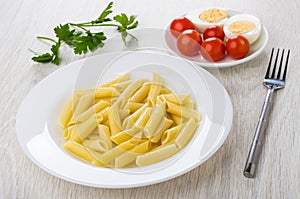 Pasta in plate, fork, tomatoes, boiled eggs in saucer, parsley