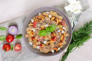 Pasta Radiatori with chicken, mushrooms, cherry tomatoes, feta cheese and tomato sauce on a light background.