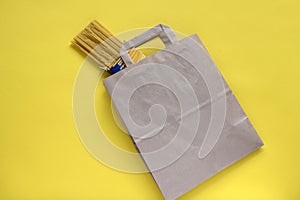 Pasta in recycled brown paper shopping bag with handle. Package on yellow background, flat lay, mockup. Food delivery.
