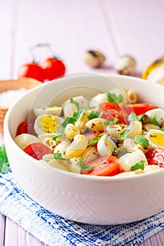 Pasta salad with quail eggs, mozzarella, cherry tomatoes and capers in bowl on purple wooden background