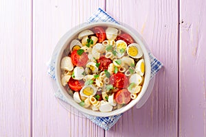 Pasta salad with quail eggs, mozzarella, cherry tomatoes and capers in bowl on purple wooden background