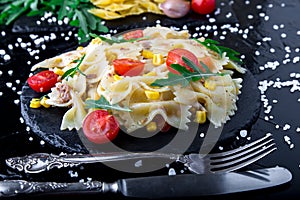 Pasta salad in slate plate with tomatoes cherry, tuna, corn and arugula. ingredients. Italian food.